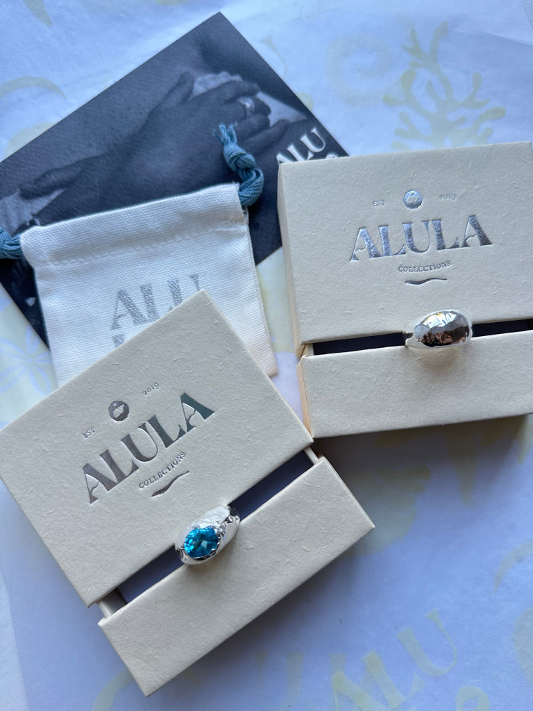 Jewelry box with a ring featuring a blue gemstone and 'ALULA' branding.