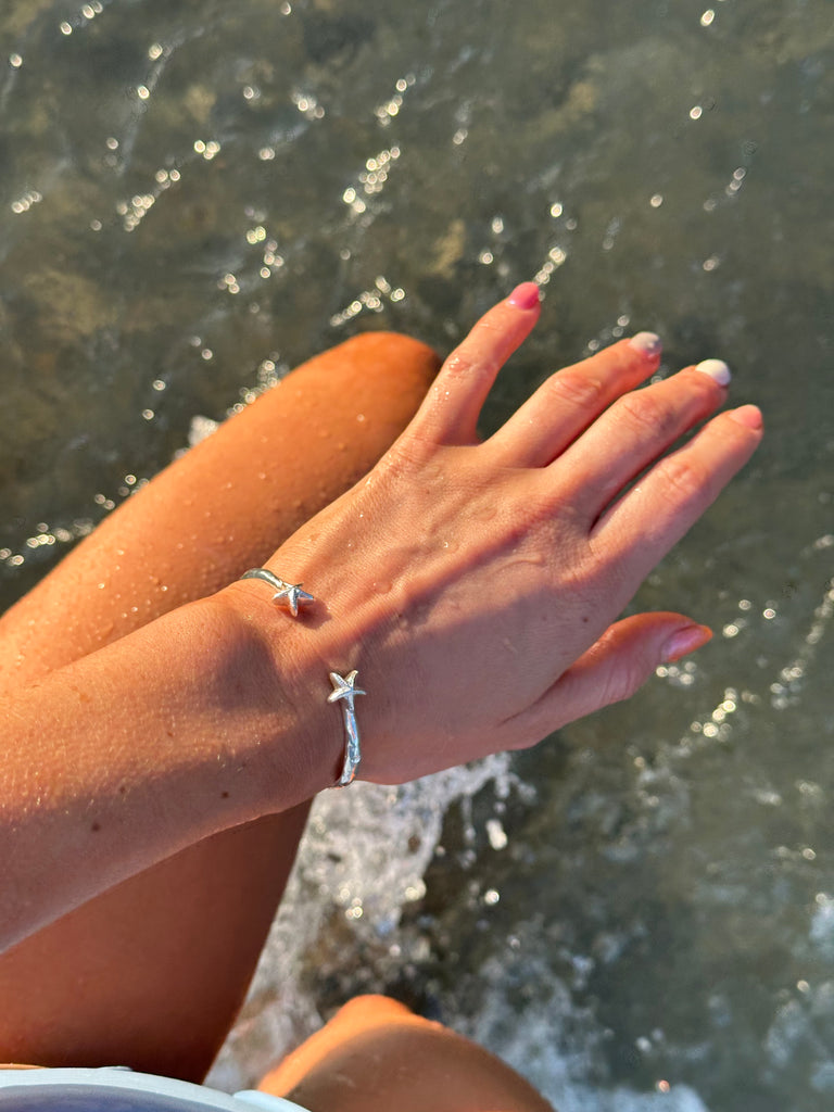 Solid 925 sterling silver starfish bangle worn on the beach, by Alula Collections Jewellery.